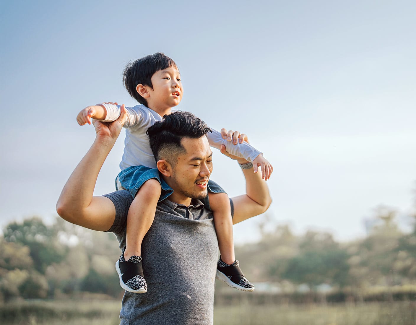 Happy father giving his young son a piggyback ride on his shoulders outdoors in a park on a sunny day.